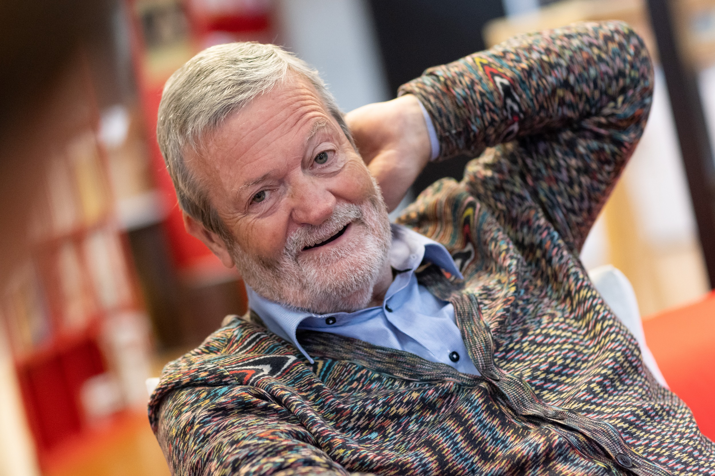 70_Jähriger im Gespräch, sich an den Hinterkopf langend