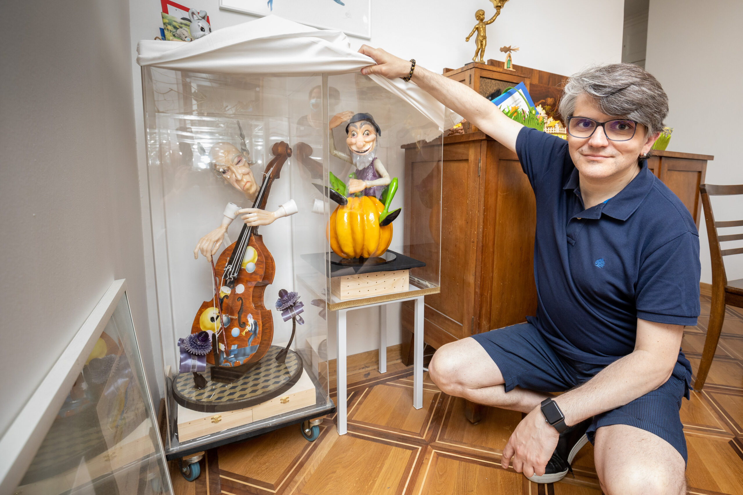 Mann in der Hocke neben zwei Vitrinen mit selbst fabrizierten, farbigen Zuckerskulpturen.