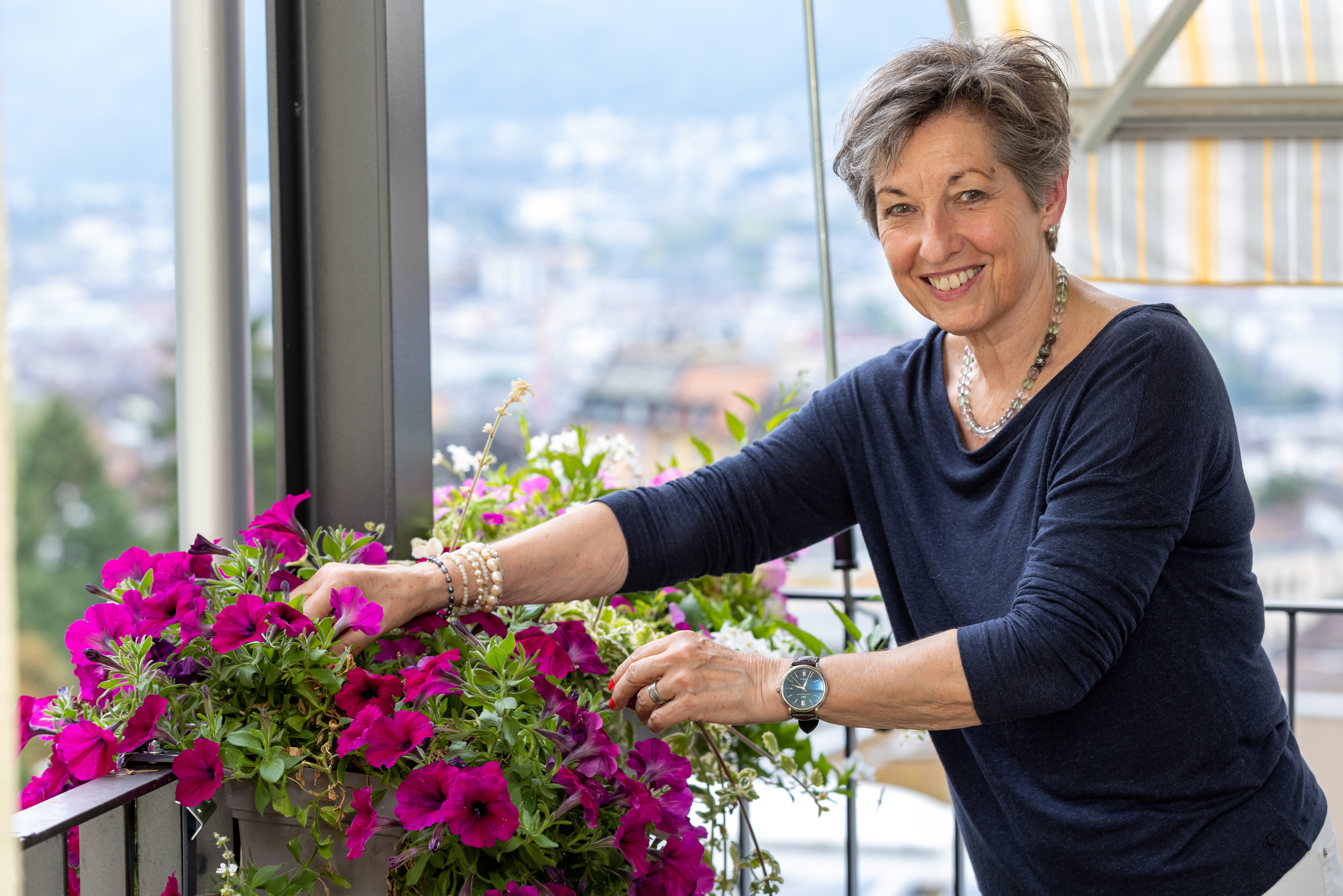 Schlanke Seniorin pflegt auf dem Balkon violett blühende Blumen.